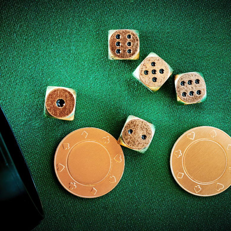 Playing in the casino and throw dice from the cup. Golden dices and chips and coins on the green textile poker table. Gambling and entertainment. Online games